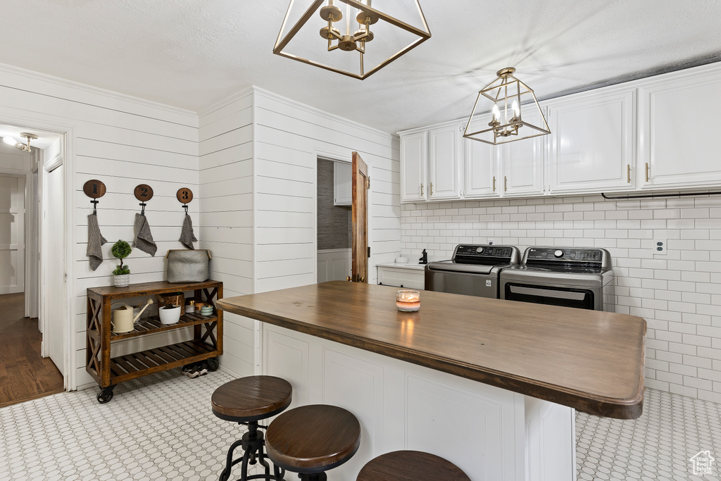 Kitchen featuring white cabinets, butcher block counters, pendant lighting, a kitchen breakfast bar, and washer and clothes dryer