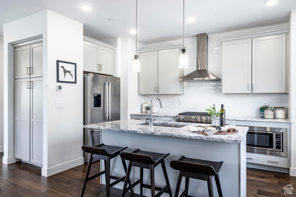 Kitchen featuring dark hardwood / wood-style floors, pendant lighting, tasteful backsplash, and wall chimney exhaust hood