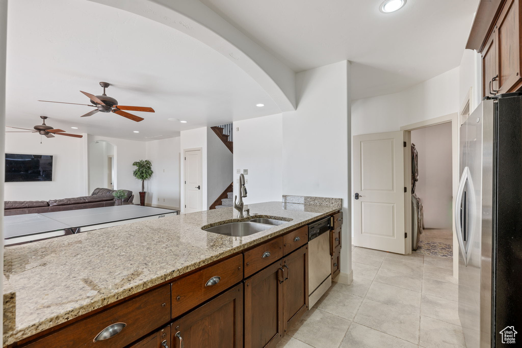 Kitchen featuring sink, stainless steel fridge, dishwashing machine, ceiling fan, and light stone counters