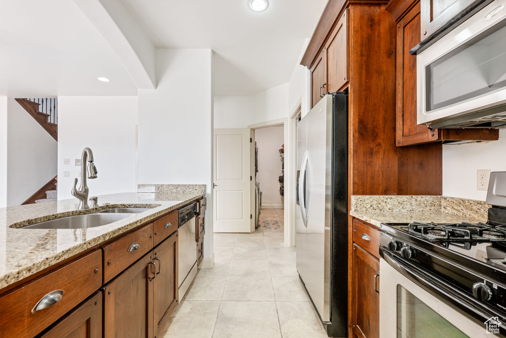 Kitchen featuring appliances with stainless steel finishes, sink, light stone counters, and light tile floors