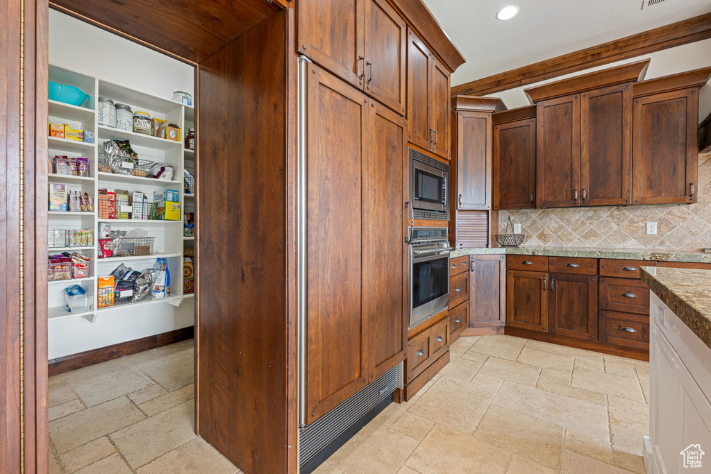 Kitchen featuring light tile flooring, light stone countertops, tasteful backsplash, and built in appliances