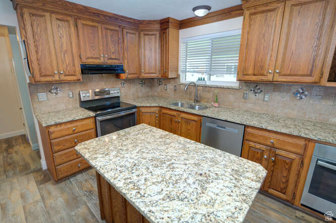 Kitchen featuring light stone countertops, sink, stainless steel appliances, and exhaust hood