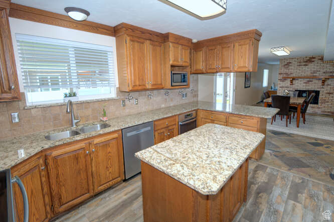 Kitchen featuring a center island, stainless steel appliances, sink, hardwood / wood-style flooring, and light stone countertops