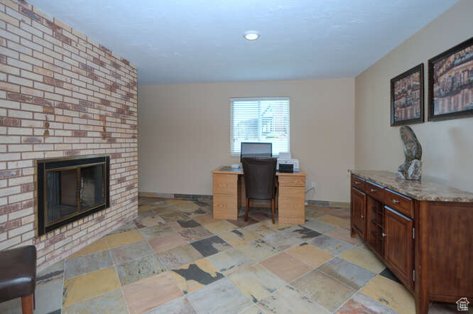 Office area featuring light tile floors, brick wall, and a fireplace