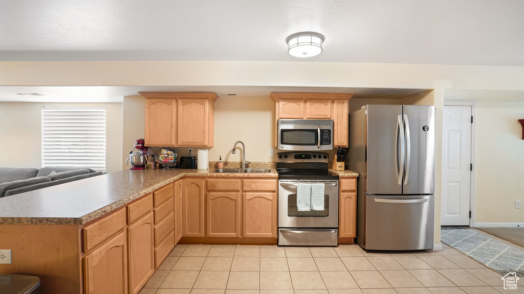 Kitchen with appliances with stainless steel finishes, sink, kitchen peninsula, and light tile floors