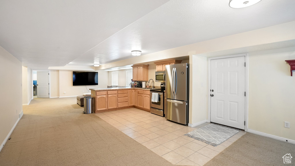 Kitchen with appliances with stainless steel finishes, light brown cabinetry, light colored carpet, and sink