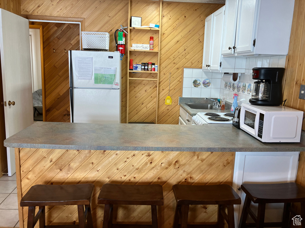 Kitchen featuring white cabinets, kitchen peninsula, backsplash, a breakfast bar area, and white appliances
