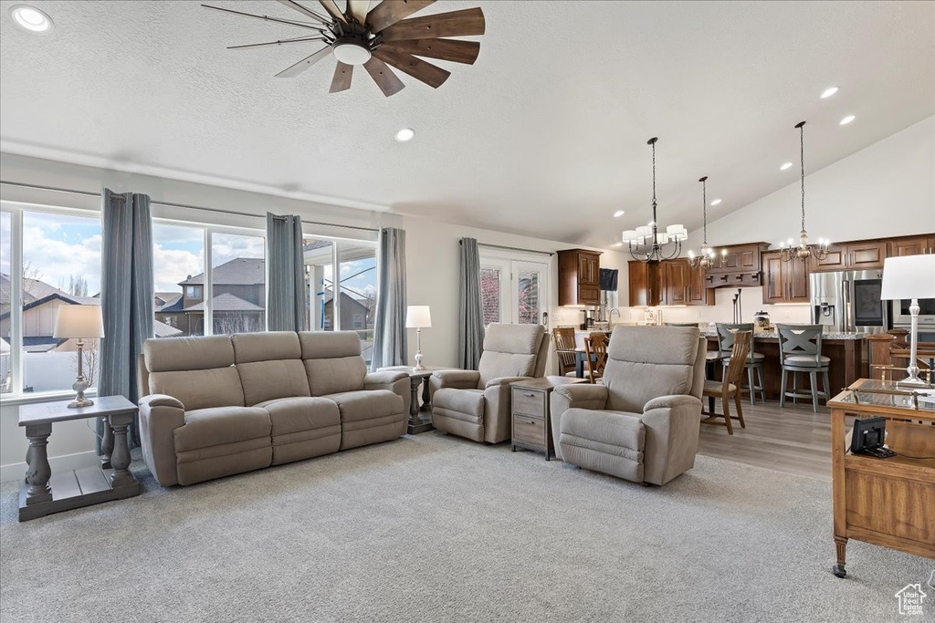 Carpeted living room featuring high vaulted ceiling and ceiling fan with notable chandelier
