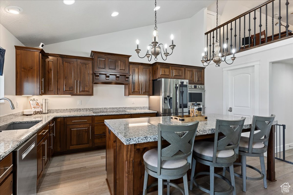 Kitchen with appliances with stainless steel finishes, a center island, ventilation hood, a chandelier, and light stone countertops