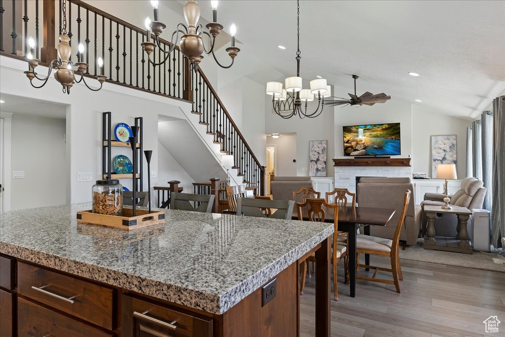 Kitchen with stone countertops, a notable chandelier, high vaulted ceiling, light hardwood / wood-style floors, and a kitchen island