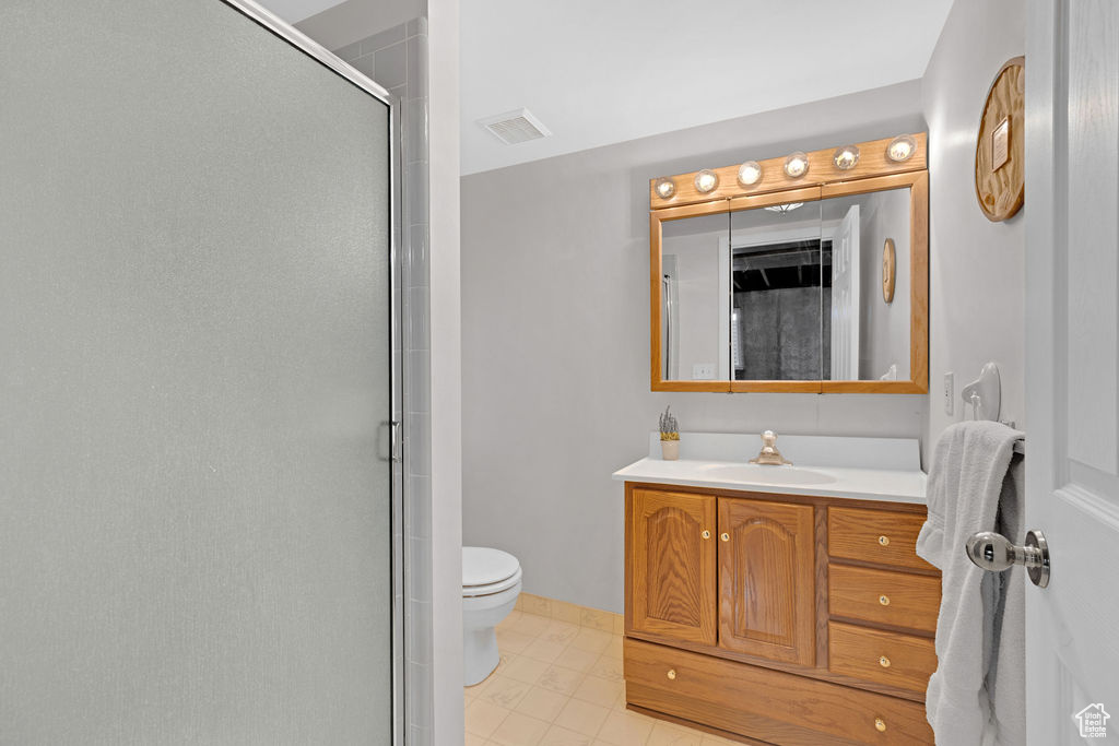 Bathroom featuring tile flooring, a shower with door, toilet, and vanity with extensive cabinet space