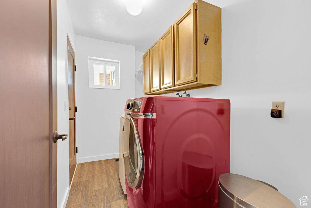 Laundry room featuring light hardwood / wood-style flooring, washing machine and clothes dryer, and cabinets