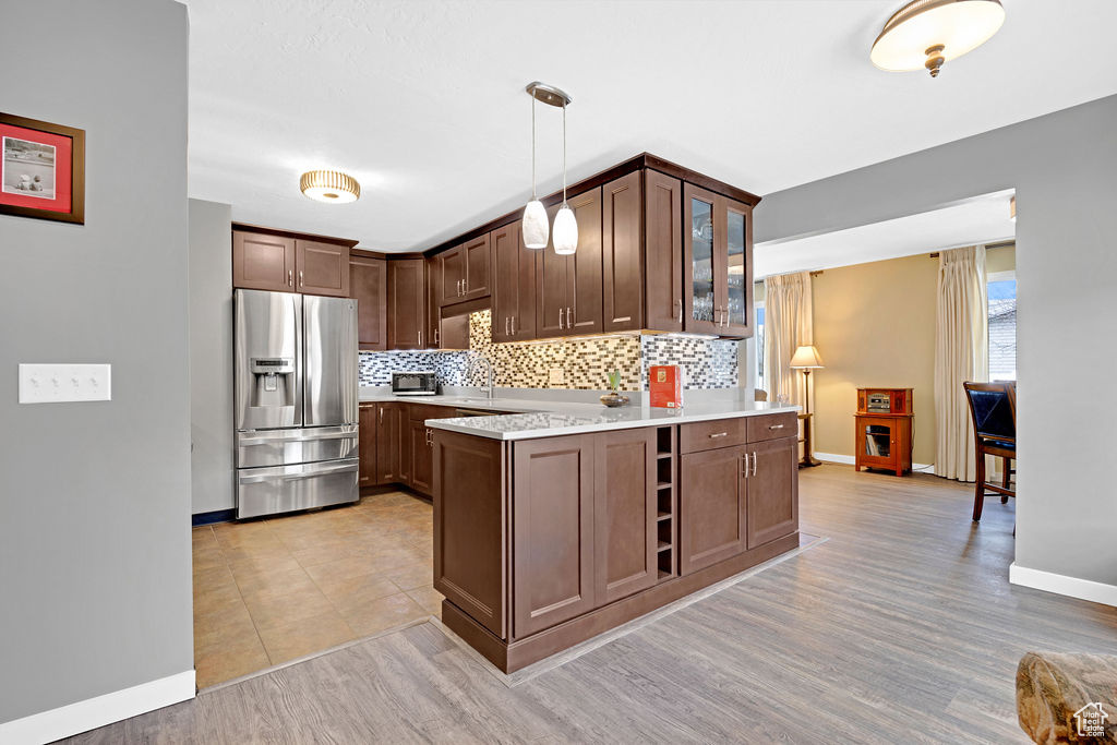 Kitchen featuring light tile floors, backsplash, dark brown cabinetry, decorative light fixtures, and stainless steel fridge with ice dispenser