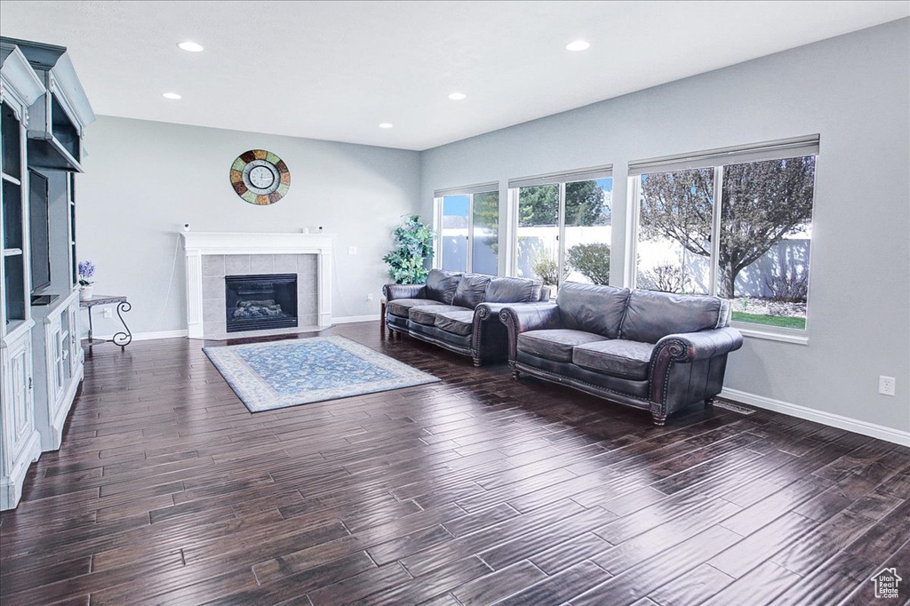 Living room with a tiled fireplace, a wealth of natural light, and dark wood-type flooring