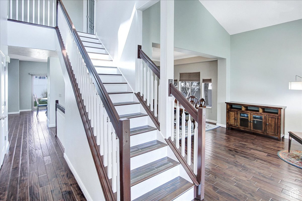 Stairway with dark hardwood / wood-style flooring and a towering ceiling