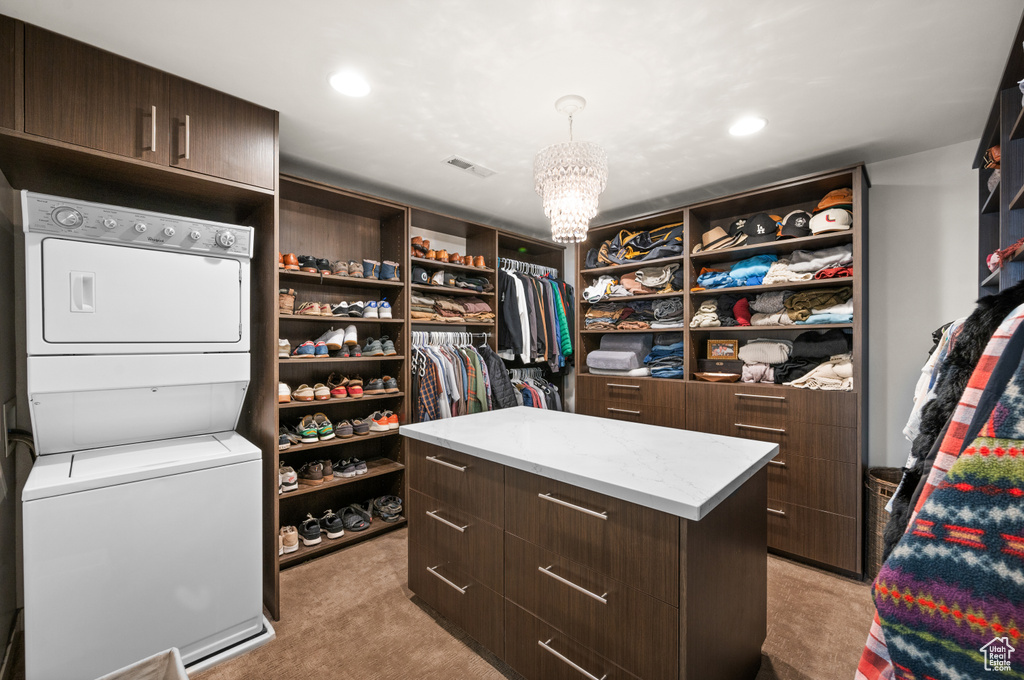 Spacious closet with an inviting chandelier, light colored carpet, and stacked washer and dryer