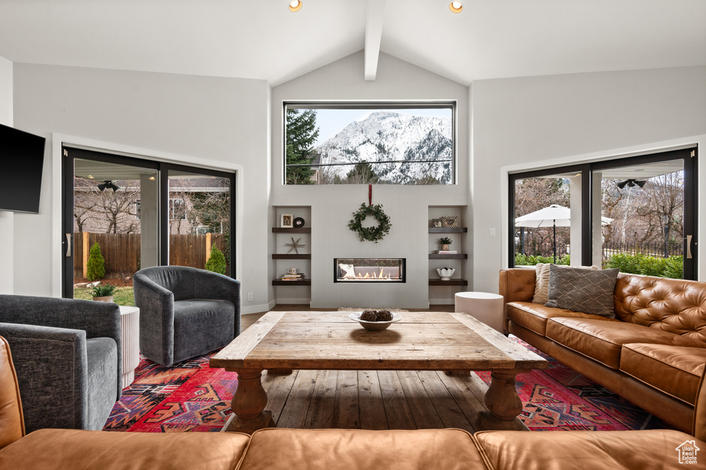 Living room featuring built in shelves, high vaulted ceiling, hardwood / wood-style flooring, and beamed ceiling
