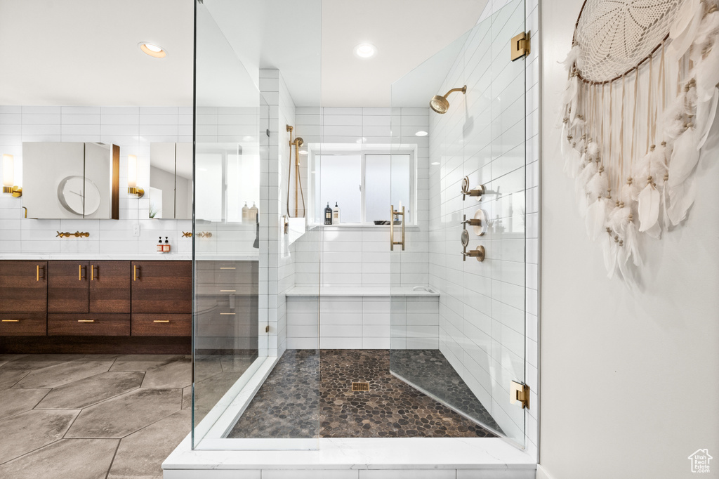 Bathroom featuring tile flooring, tile walls, a shower with door, and vanity