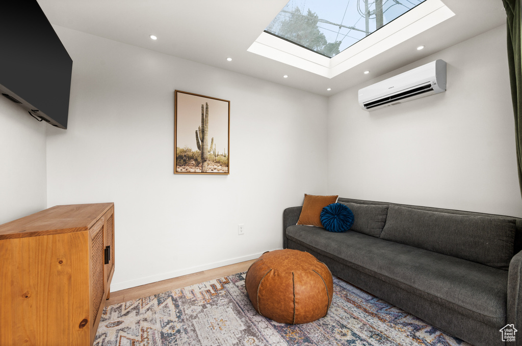 Living room with a skylight, a wall unit AC, and light hardwood / wood-style floors