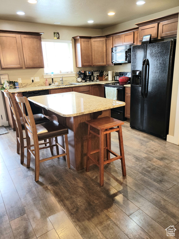 Kitchen featuring dark wood-type flooring, light stone counters, a center island, a kitchen breakfast bar, and black appliances
