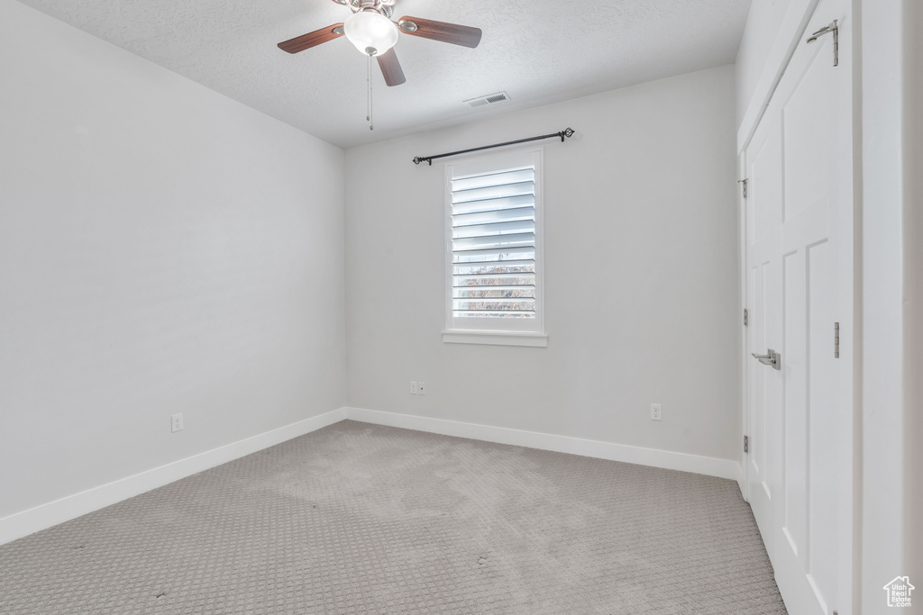 Unfurnished bedroom with ceiling fan, a textured ceiling, and light carpet