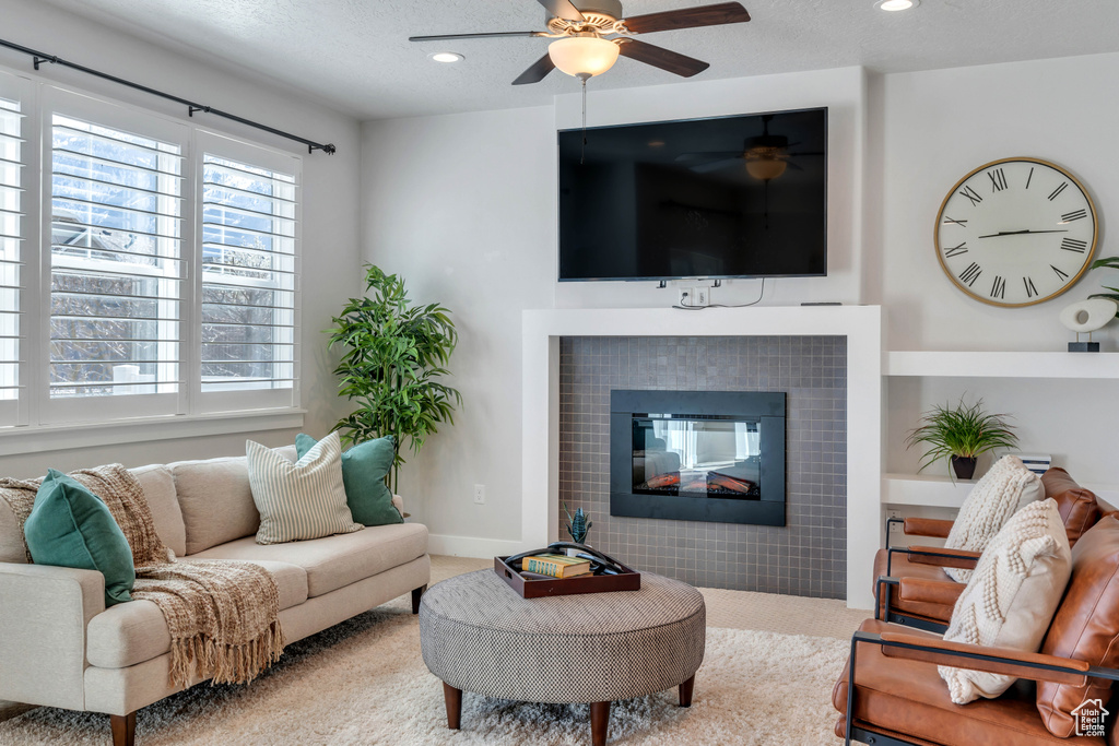 Carpeted living room featuring ceiling fan, a textured ceiling, and a tiled fireplace