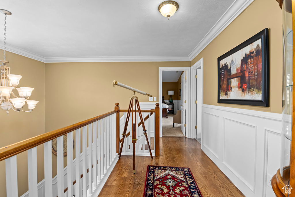 Hallway featuring an inviting chandelier, crown molding, and hardwood / wood-style floors