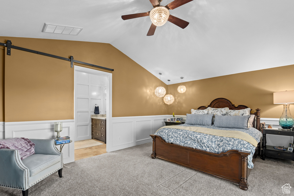 Carpeted bedroom featuring a barn door, ceiling fan, ensuite bath, and vaulted ceiling