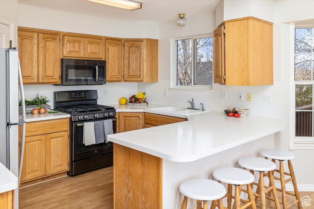 Kitchen featuring a kitchen breakfast bar, sink, kitchen peninsula, light hardwood / wood-style flooring, and black appliances