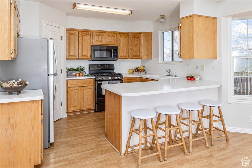 Kitchen with a breakfast bar, light hardwood / wood-style floors, kitchen peninsula, black appliances, and sink