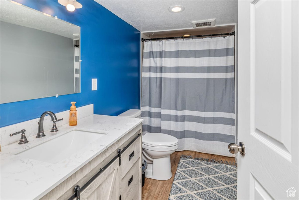 Bathroom featuring hardwood / wood-style floors, a textured ceiling, toilet, and vanity with extensive cabinet space