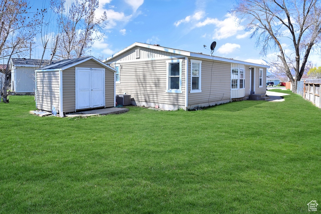 Rear view of property featuring a storage unit, a lawn, and central air condition unit