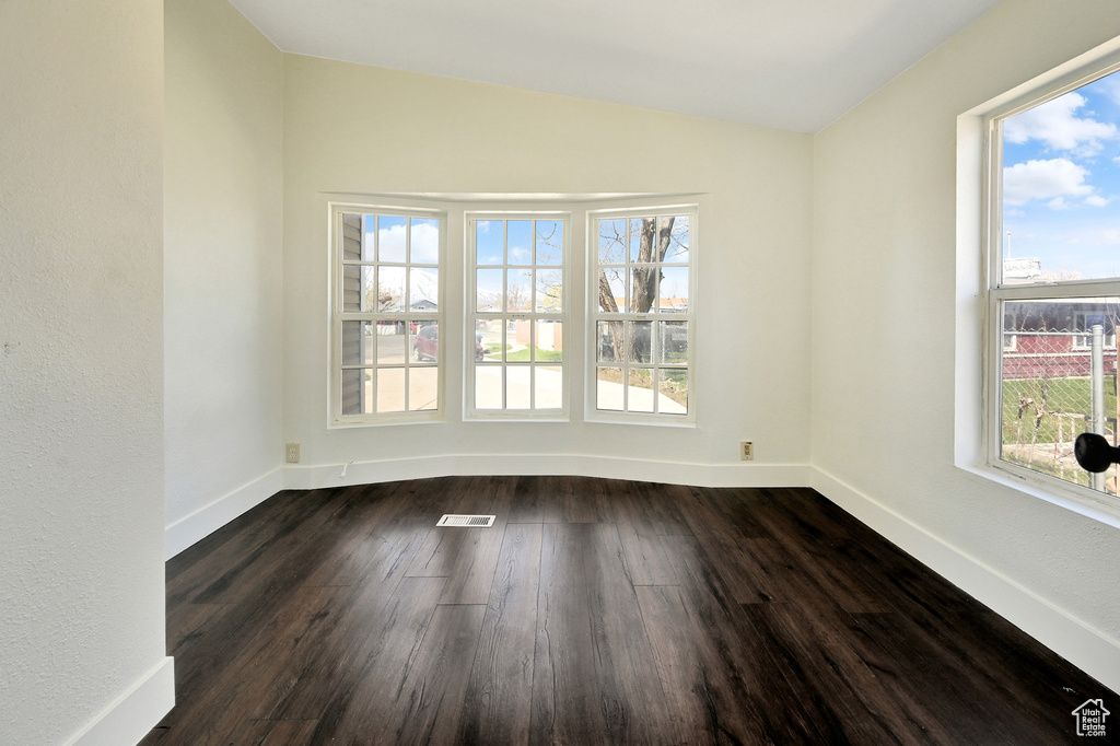 Spare room with dark hardwood / wood-style floors, a healthy amount of sunlight, and vaulted ceiling