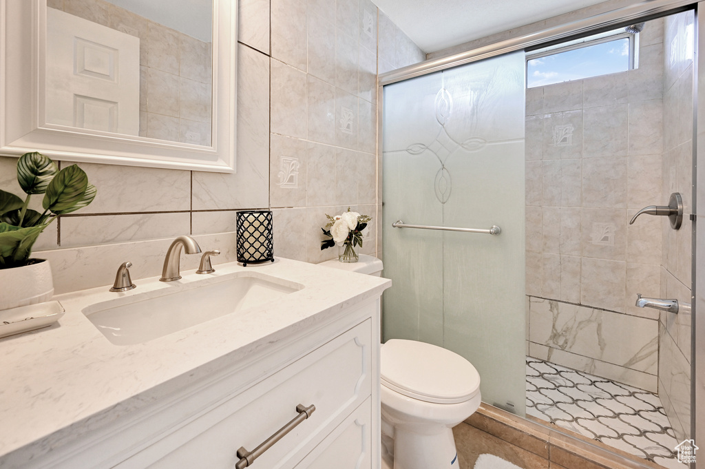 Bathroom with toilet, large vanity, tile walls, tile flooring, and an enclosed shower