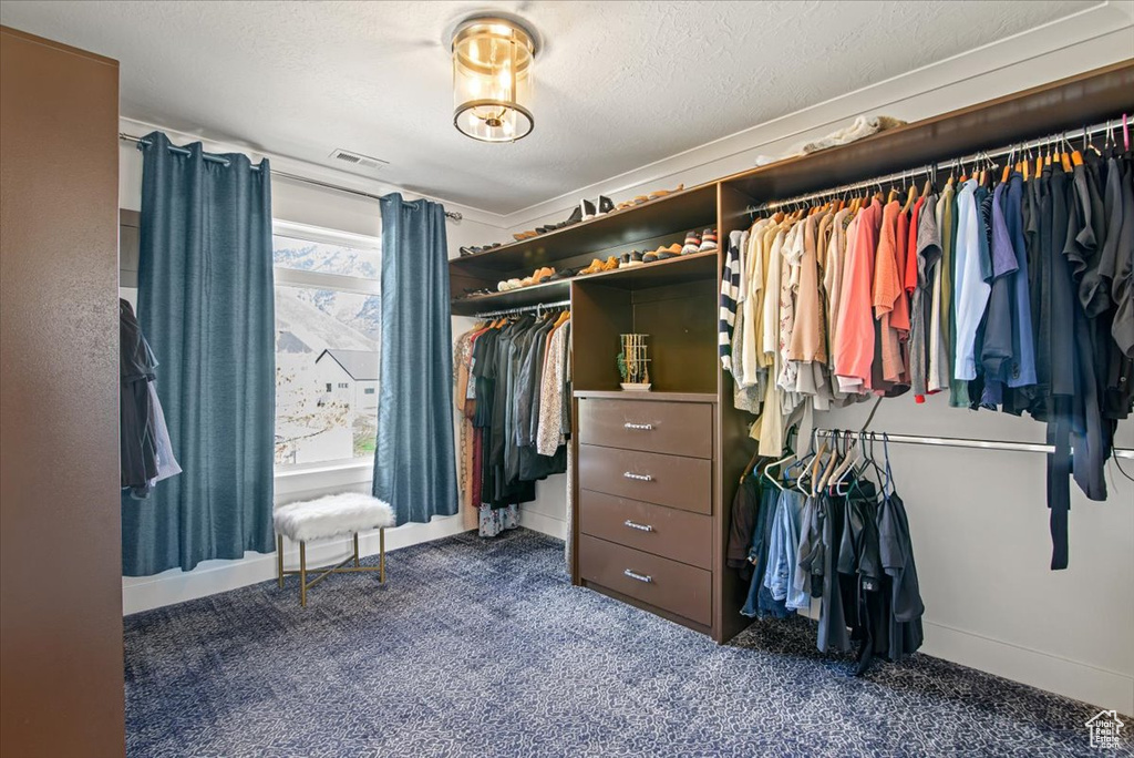 Spacious closet featuring dark carpet and a notable chandelier