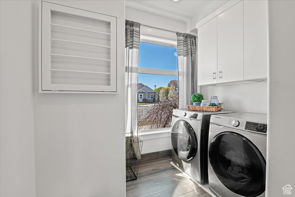 Laundry room with independent washer and dryer, hardwood / wood-style flooring, and cabinets