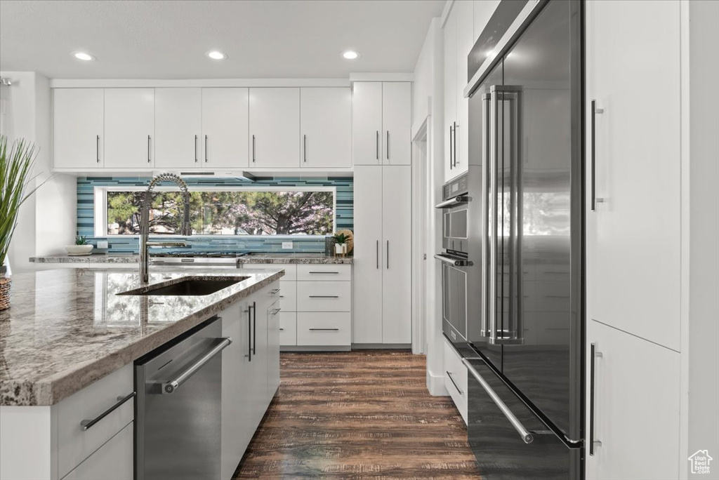 Kitchen featuring stainless steel appliances, dark wood-type flooring, sink, light stone countertops, and white cabinetry