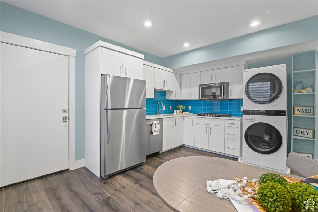 Kitchen featuring stainless steel appliances, white cabinets, sink, dark hardwood / wood-style flooring, and stacked washer and clothes dryer