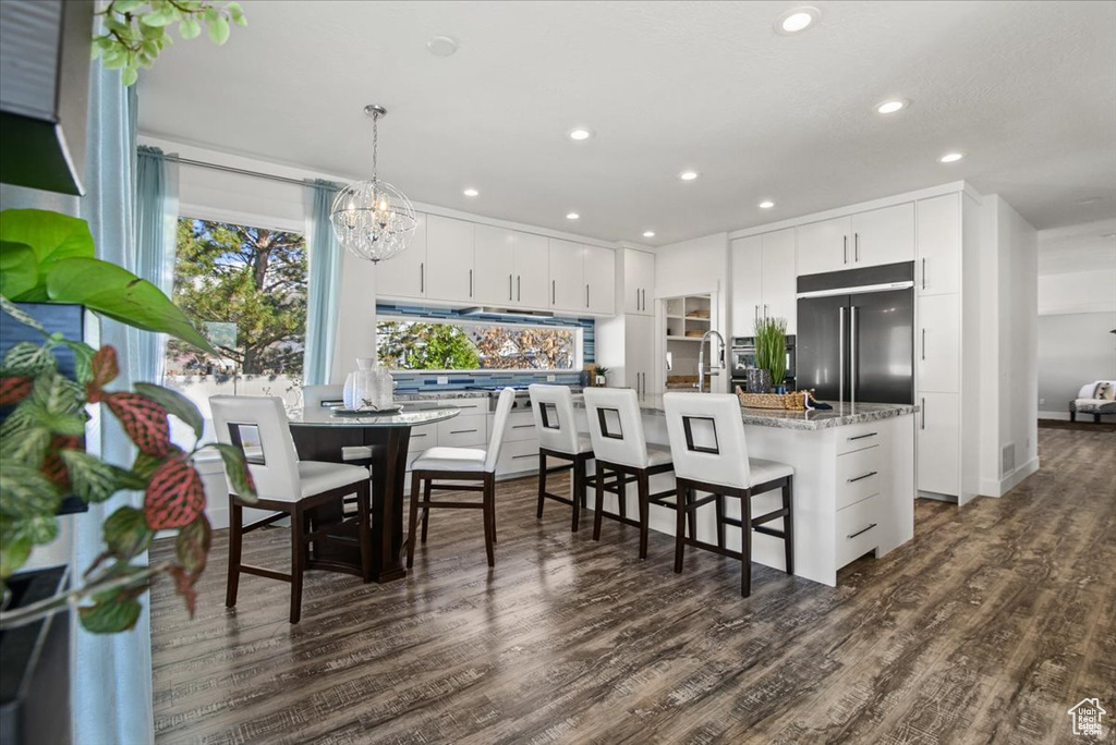 Kitchen featuring dark hardwood / wood-style flooring, a breakfast bar, hanging light fixtures, and stainless steel built in refrigerator