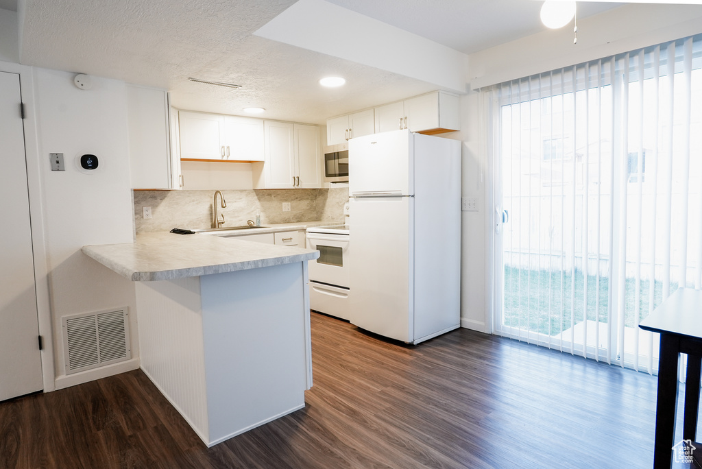 Kitchen with dark wood-type flooring, kitchen peninsula, white cabinetry, white appliances, and tasteful backsplash