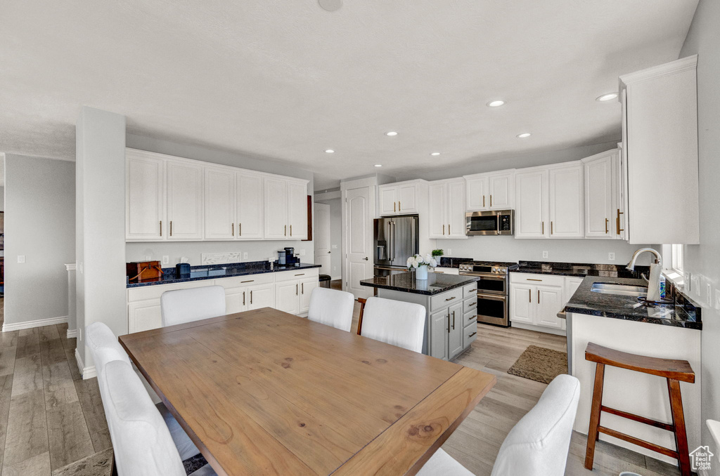 Kitchen featuring a center island, sink, light hardwood / wood-style floors, white cabinetry, and stainless steel appliances