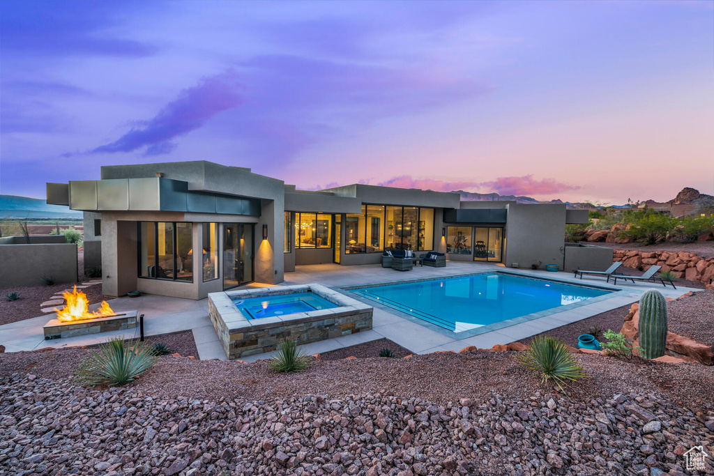 Pool at dusk featuring a patio, an outdoor fire pit, and an in ground hot tub