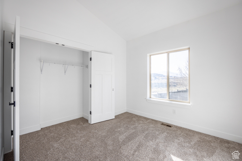 Unfurnished bedroom with a closet, light colored carpet, and vaulted ceiling