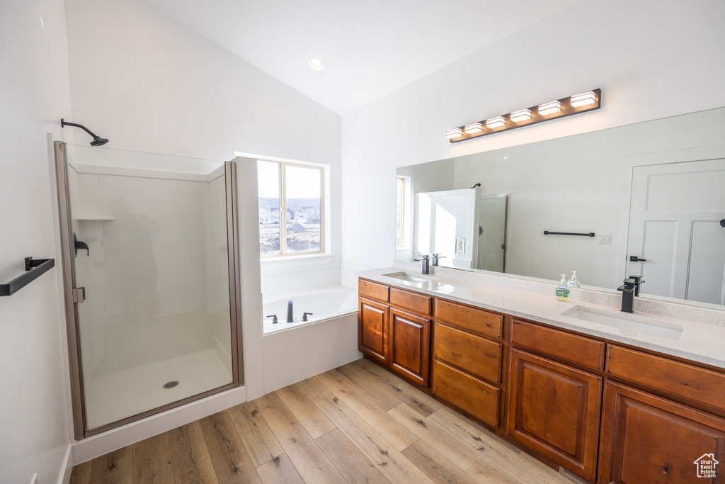 Bathroom featuring hardwood / wood-style flooring, independent shower and bath, vaulted ceiling, and dual bowl vanity