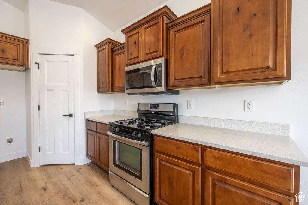 Kitchen with appliances with stainless steel finishes, light stone counters, and light hardwood / wood-style flooring