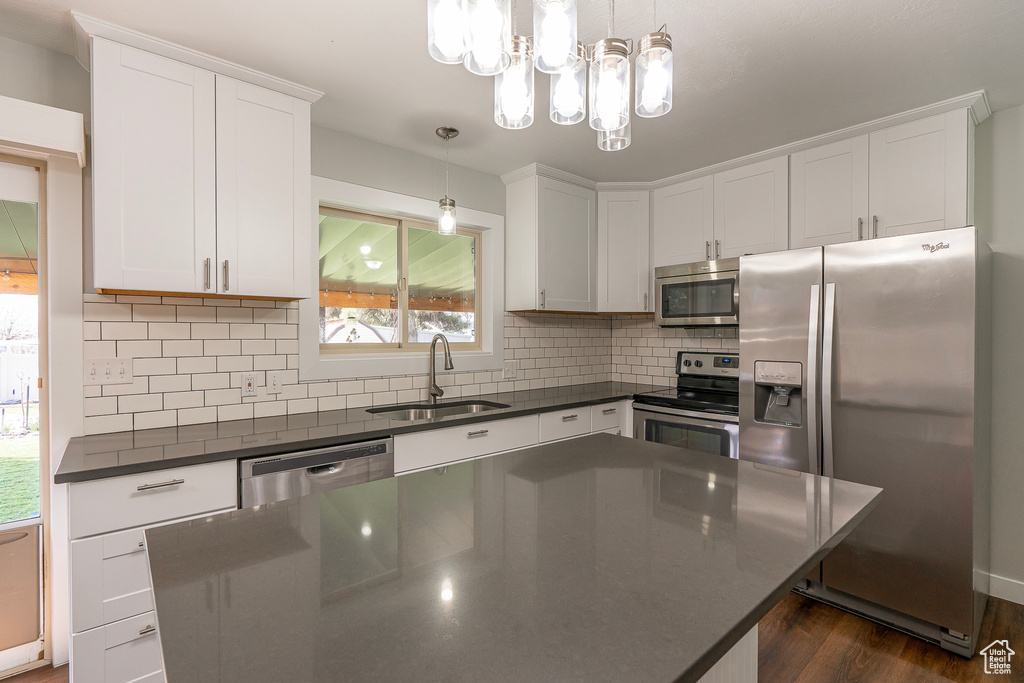 Kitchen with appliances with stainless steel finishes, sink, white cabinetry, and decorative light fixtures