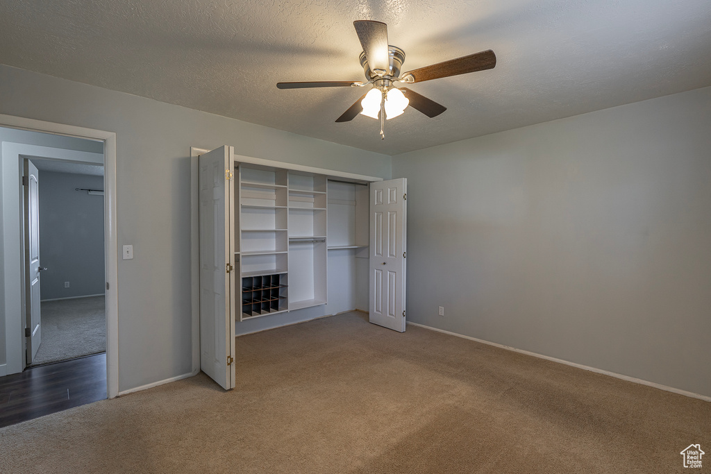 Unfurnished bedroom with ceiling fan, a textured ceiling, dark colored carpet, and a closet