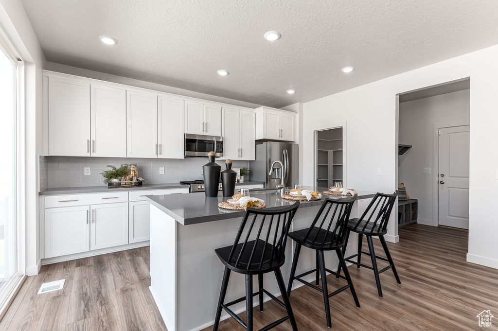 Kitchen with stainless steel appliances, white cabinets, a kitchen breakfast bar, a kitchen island with sink, and hardwood / wood-style floors