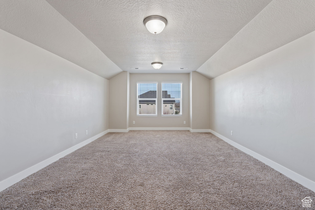 Empty room featuring a textured ceiling, carpet floors, and vaulted ceiling
