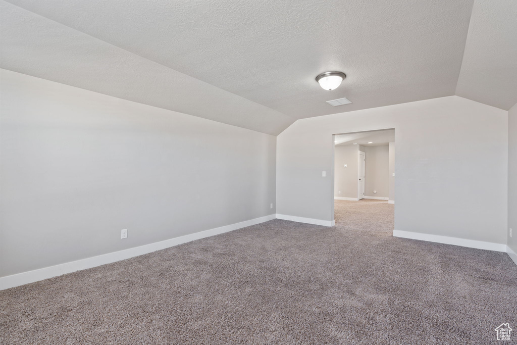Spare room with a textured ceiling, vaulted ceiling, and carpet